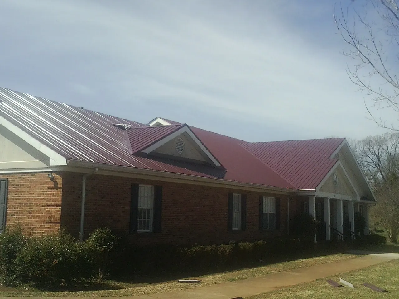 Red metal roof with gabled entries on a long brick building, from a Hail Damage Roof Repair job in Tallahassee