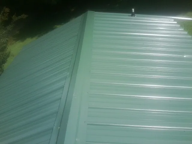 New green metal panels meeting at the ridge of a roof — Flat Roof Repair work by our crew in Tallahassee