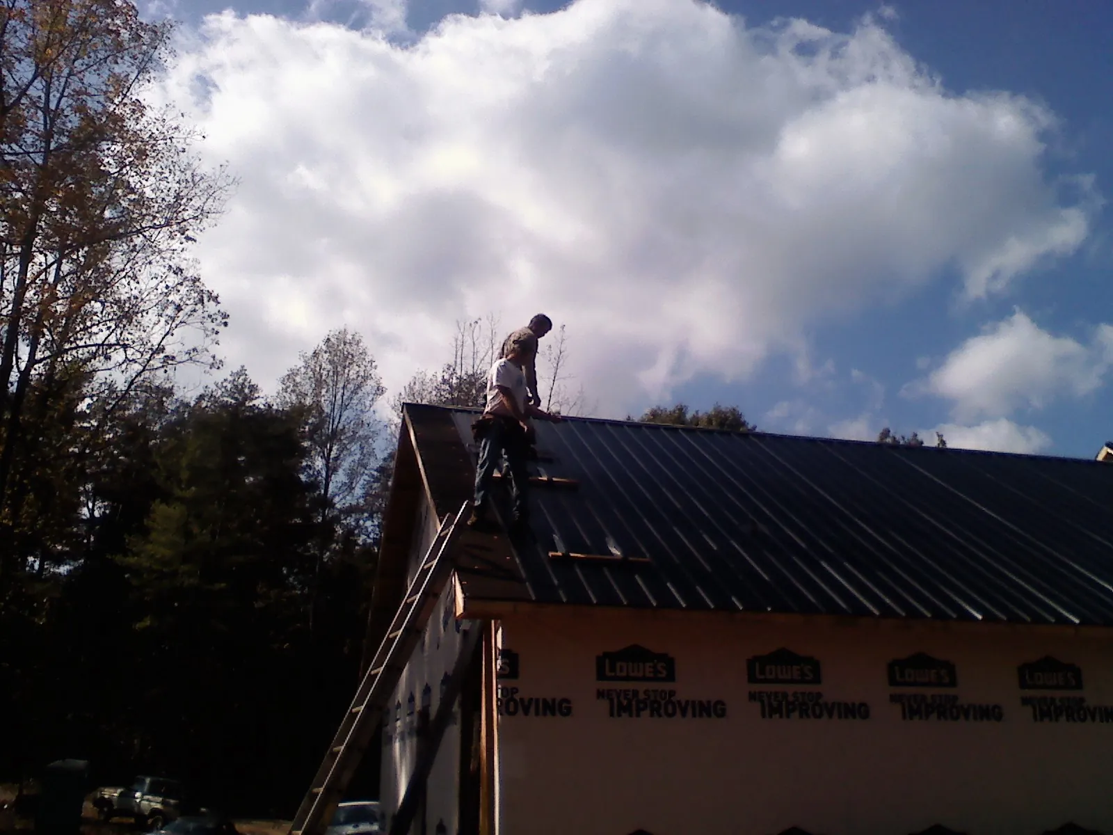 Roofer fastening dark metal panels high against a cloudy sky, from a Roof Inspection job in Tallahassee