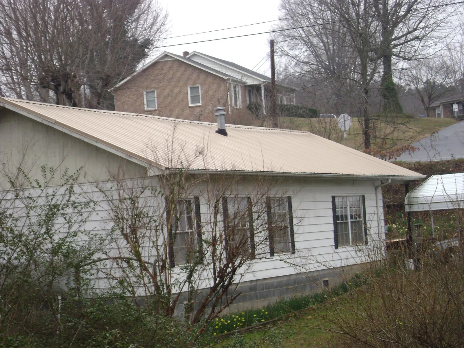 Tan metal roof on a white sided house set into a hillside — Commercial Roofing by Roofing Brothers in Tallahassee